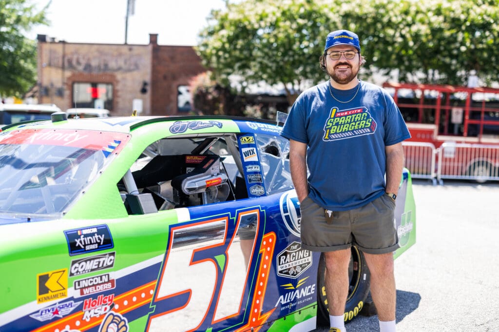 Arrowhead Design Group designer and illustrator Will Mathis stands in front of Jeremy Clements' NASCAR car at Rockers Brewing Co. in Spartanburg, SC.